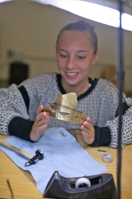 student holds piece of jewelry she designed