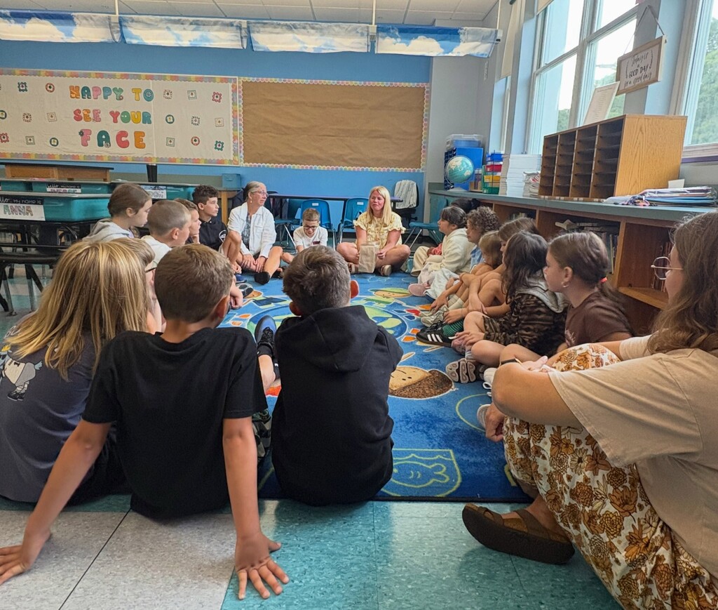 students sit around rug in classroom