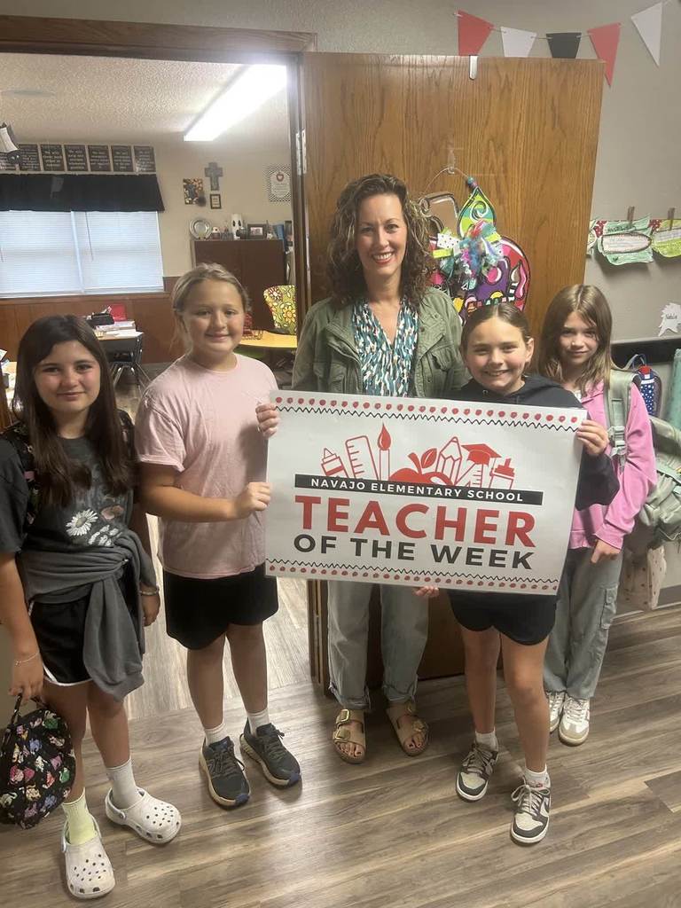 Mrs Funkhouser with 4 6th grade girls holding a teach of the week sign in front of her classroom door. 
