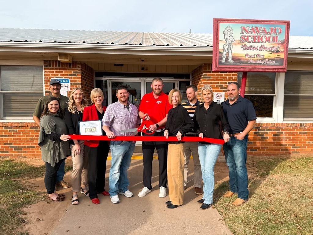 Ribbon cutting in front of the Navajo High School Doors. In the middle is Mr. Granger holder large red scissors cutting the ribbon.