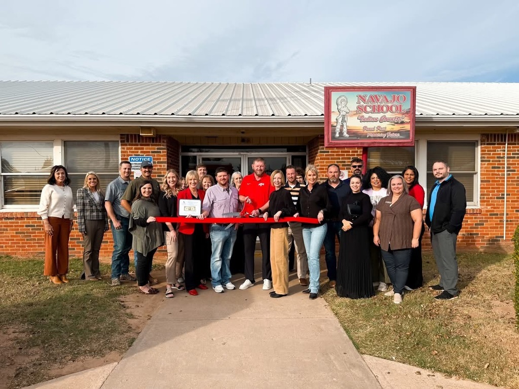 A large group of people standing with Mr. granger in front of the high school entrance as he cuts the ribbon.