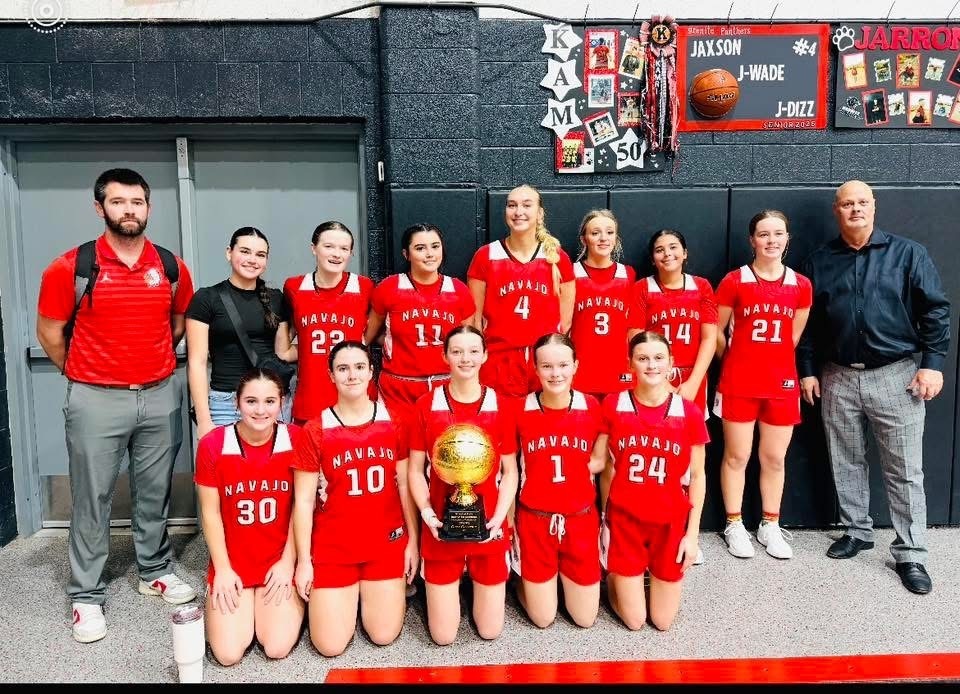 Girls basketball team holding a large gold 1st place basketball trophy