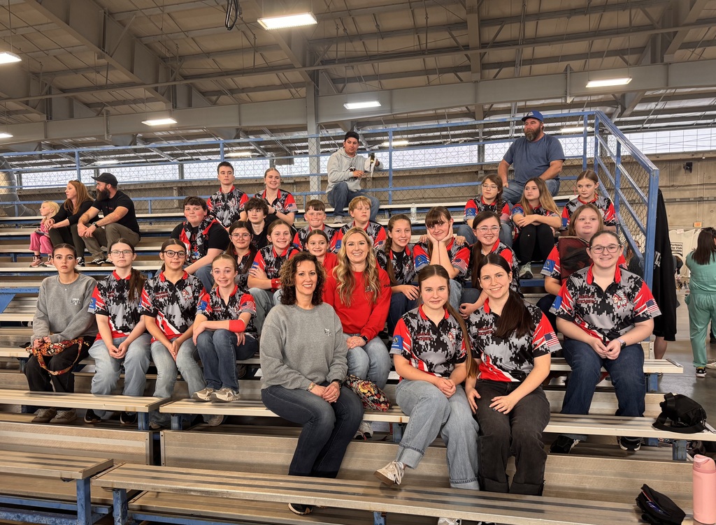 Archery team and coaches siting on bleachers inside of the venue waiting for their turn.