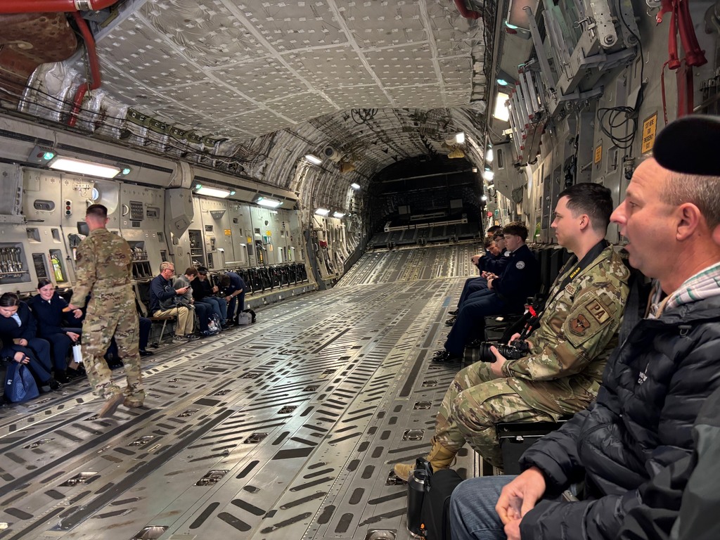 Inside the back on a C-17, guests are sitting in jump seats along both sides of the airplane. 