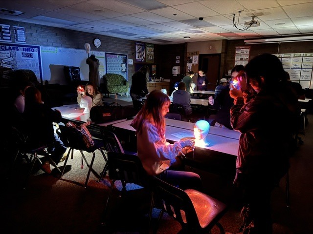 The drama tech students are using flashlights and colored gels to establish the perfect colors and angles of light to fit their chosen genres.