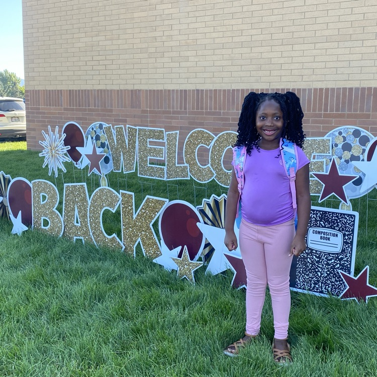 student standing in front of a sign that says welcome back