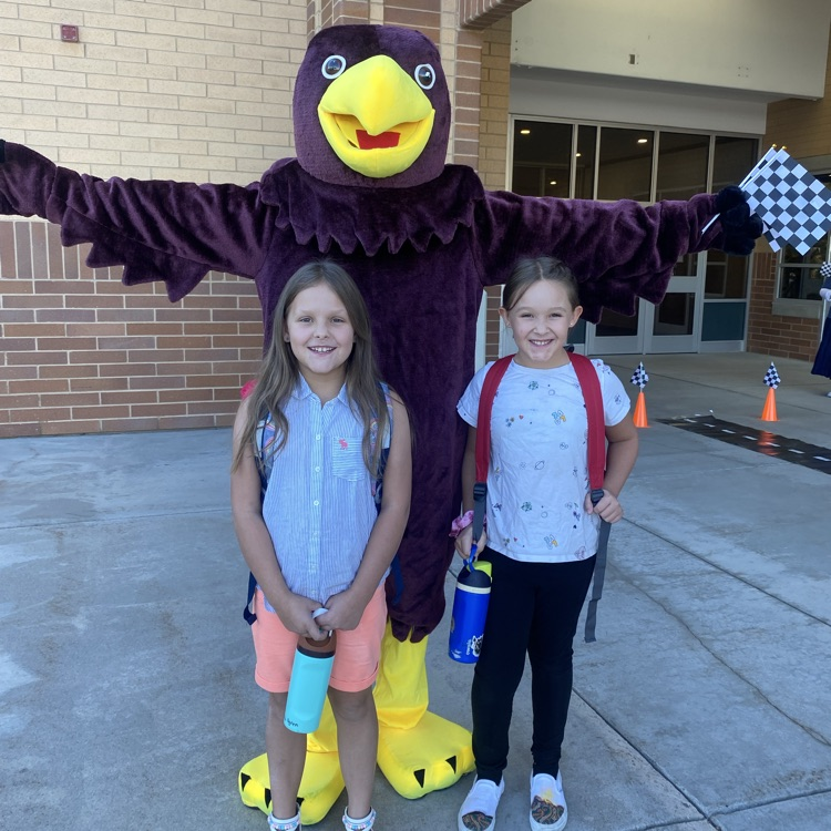 two students standing in front of a Hawk mascot