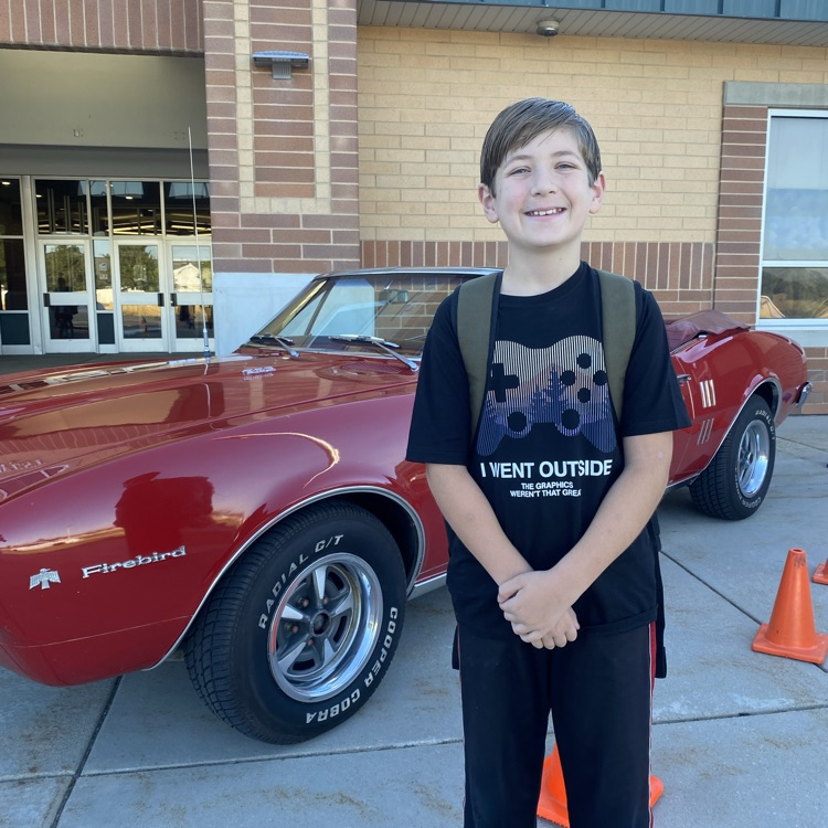 a boy standing in front of a red firebird car