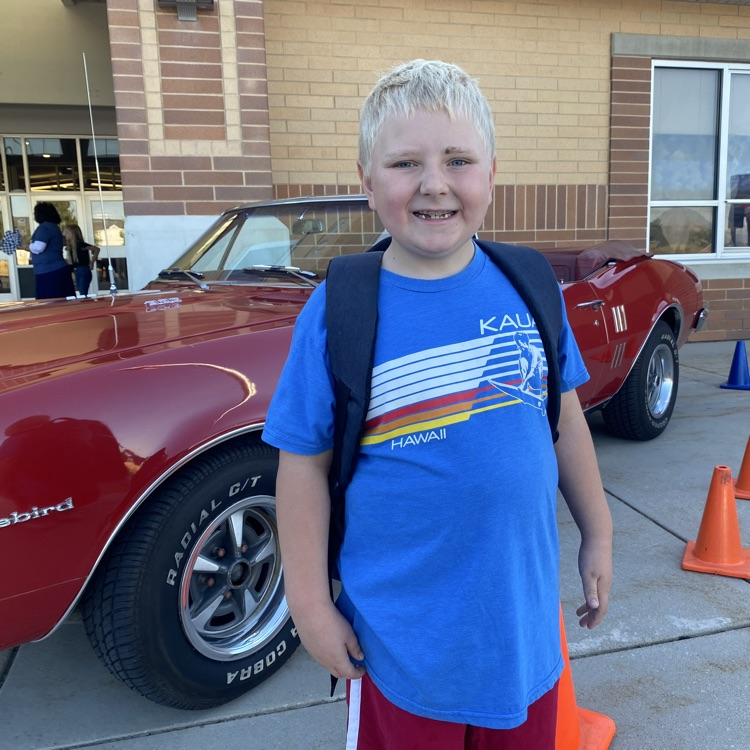 a young boy standing in front of a red firebird car