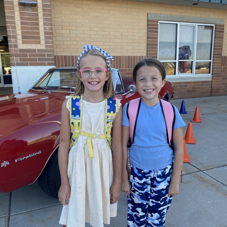 two students standing in front of a red car