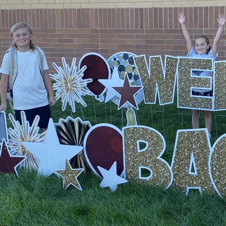 two students standing next to a welcome back sign