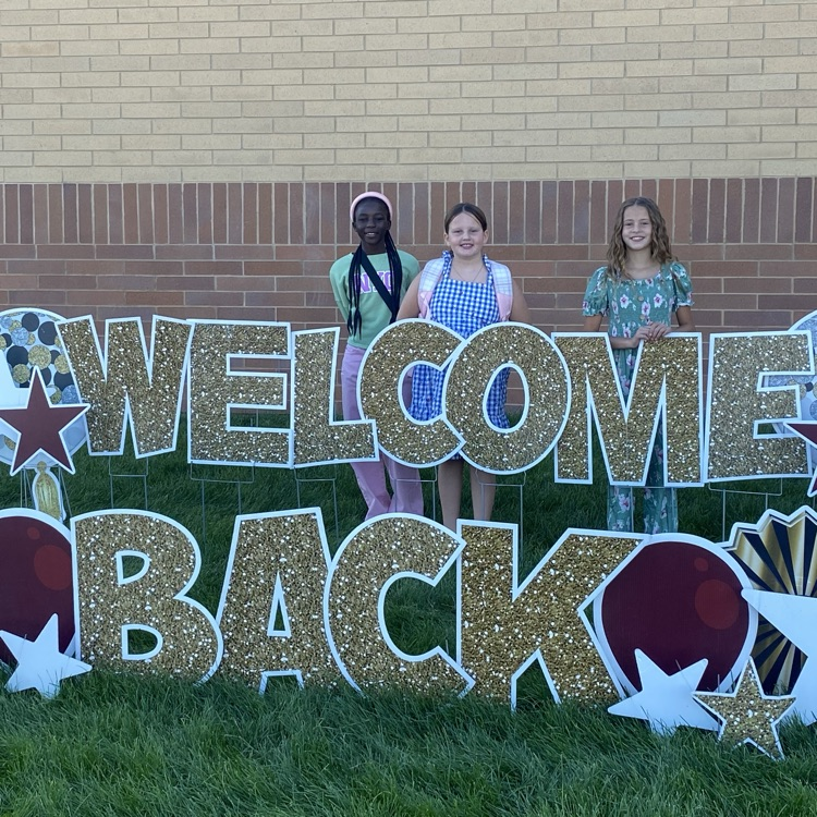 three girls standing in front of a welcome back sign