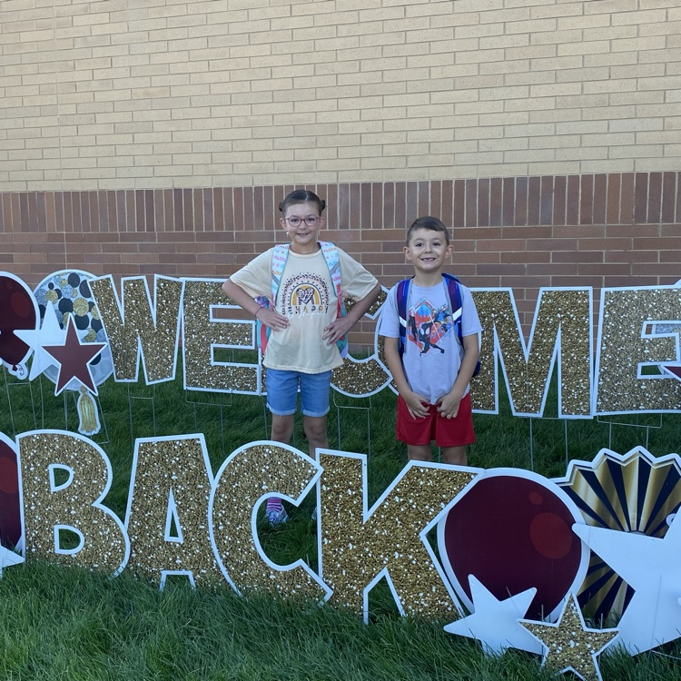 two students standing in front of a welcome back sign