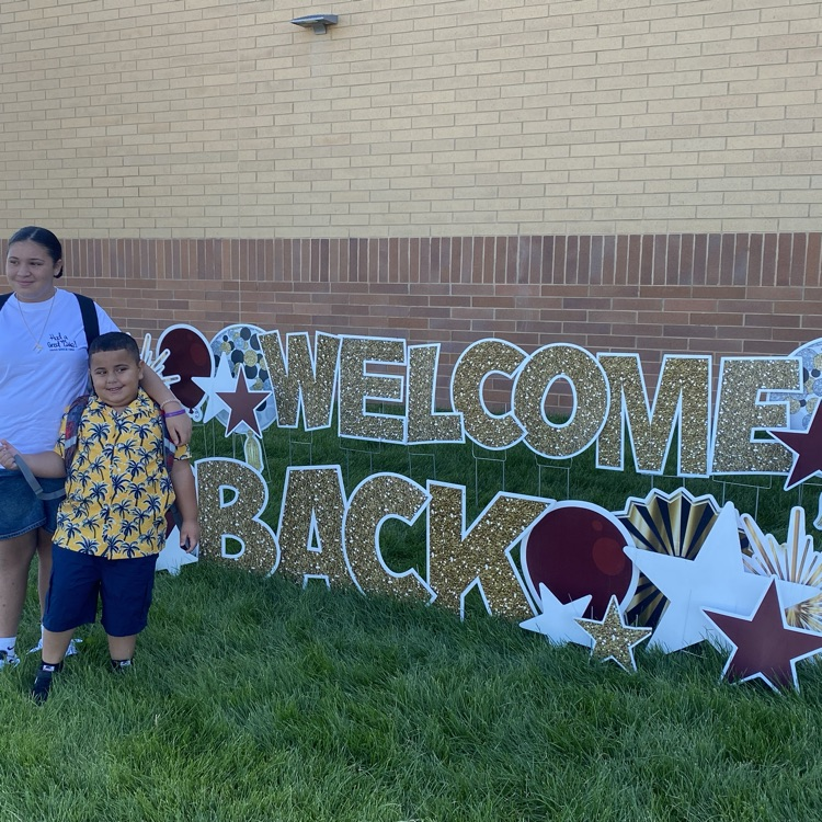 a brother and sister standing in front of a welcome back sign