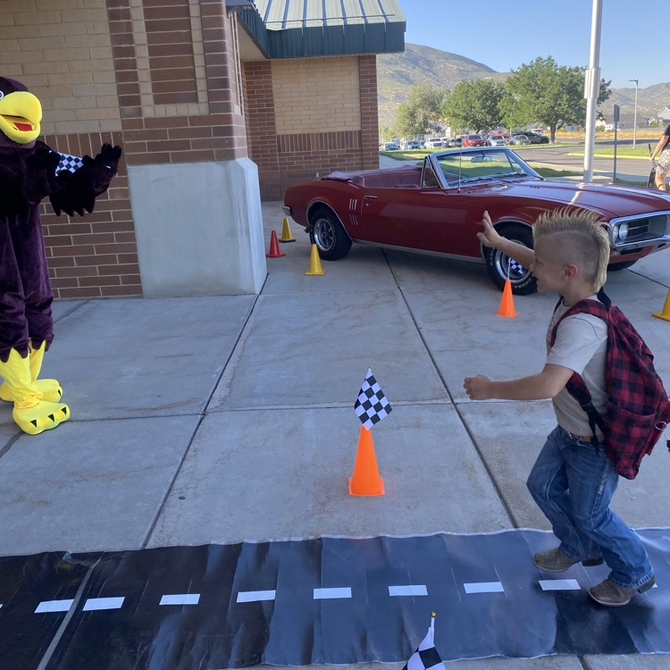 a boy waving to a hawk mascot with a red car in the background