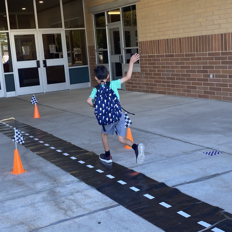 young boy waving goodbye as he runs into the school