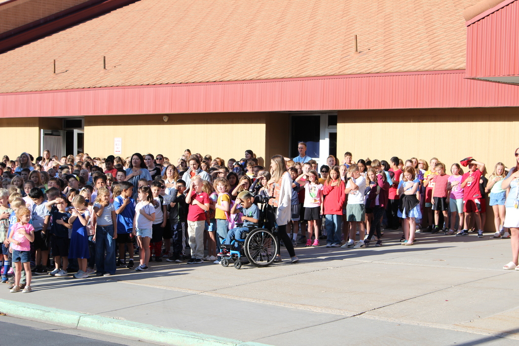 Students and teachers with hands on hearts watching the raising of the flag