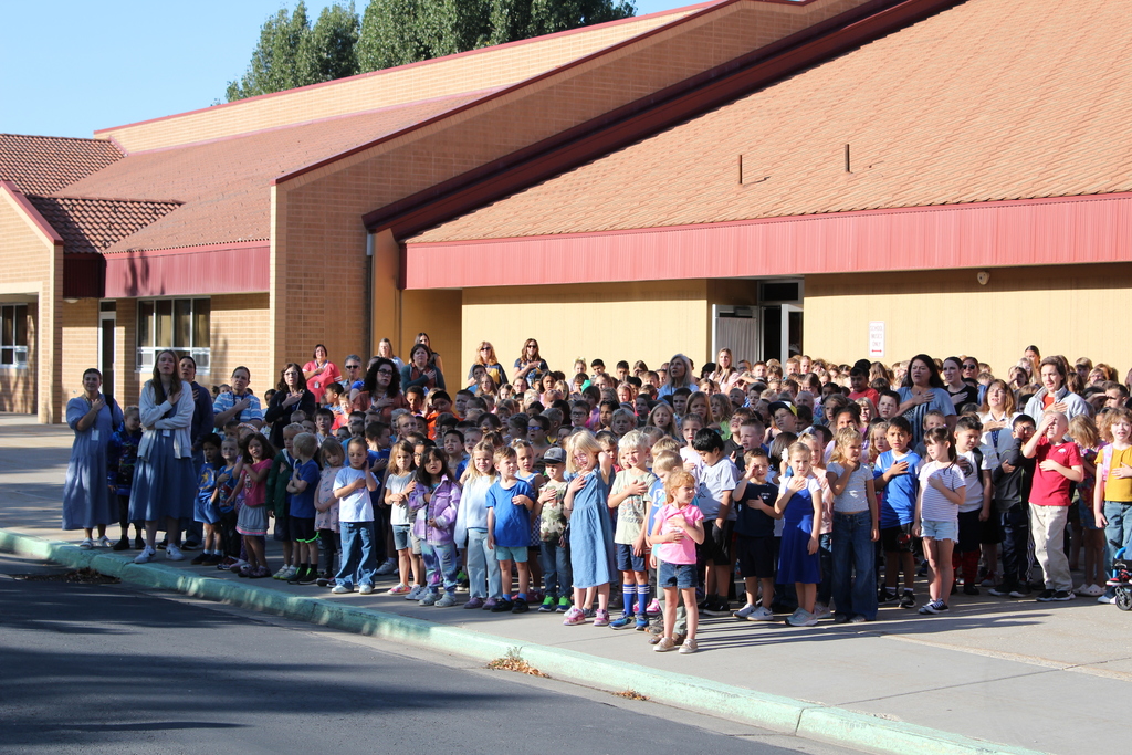 Students and teachers with hands on hearts watching the raising of the flag