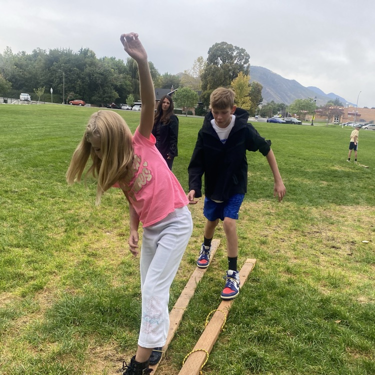 two students showing teamwork by walking on pieces of wood