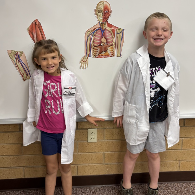 two students with doctor coats stand in front of a whiteboard with a skeleton magnet
