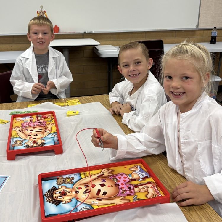 3 students wearing white coats playing operation
