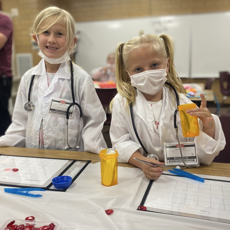 two students in white coats with pretend medicine bottles