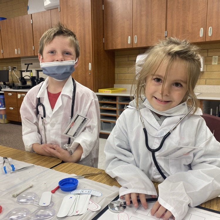 two kids in white coats. one in a medical mask. one with a stethoscope