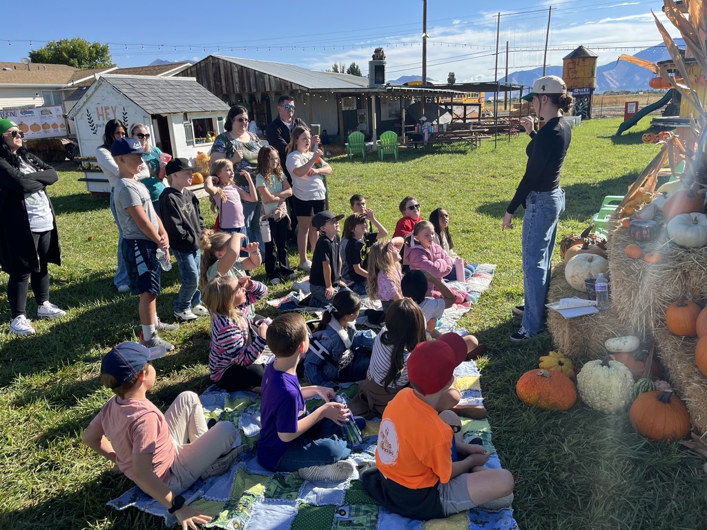 a class of students sitting on the grass and listening to a presentation