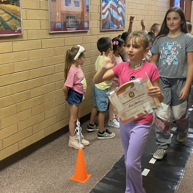 a student waving while other kids cheer for her