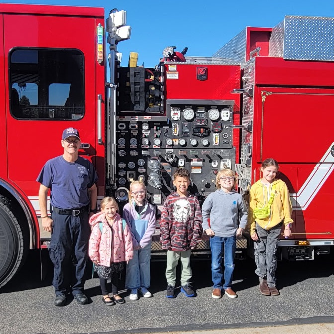 five students standing next to a firefighter in front of a fire truck