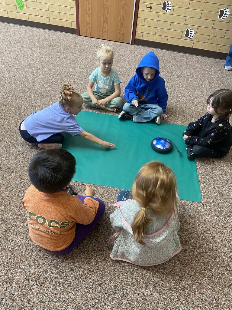 6 students sitting around a blue piece of fabric with a hoverboard in the middle of them