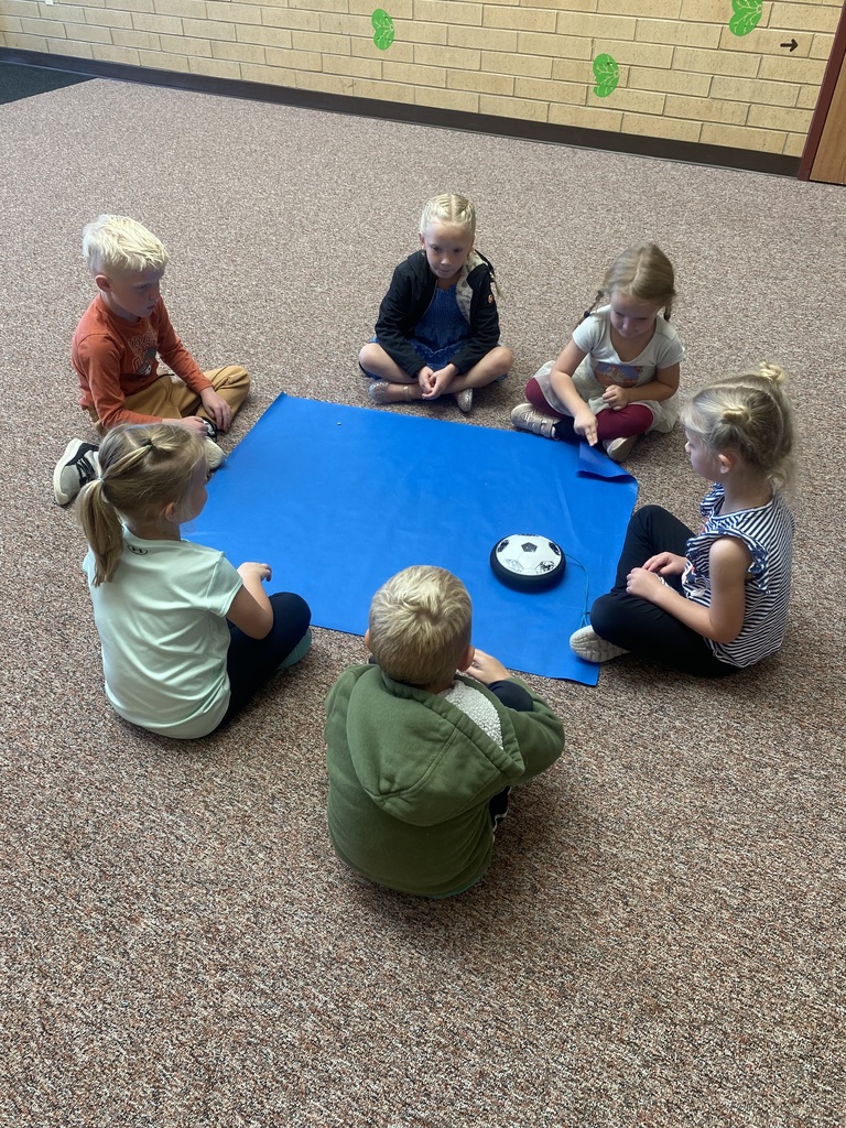 6 students sitting around a blue piece of fabric with a hoverboard in the middle of them