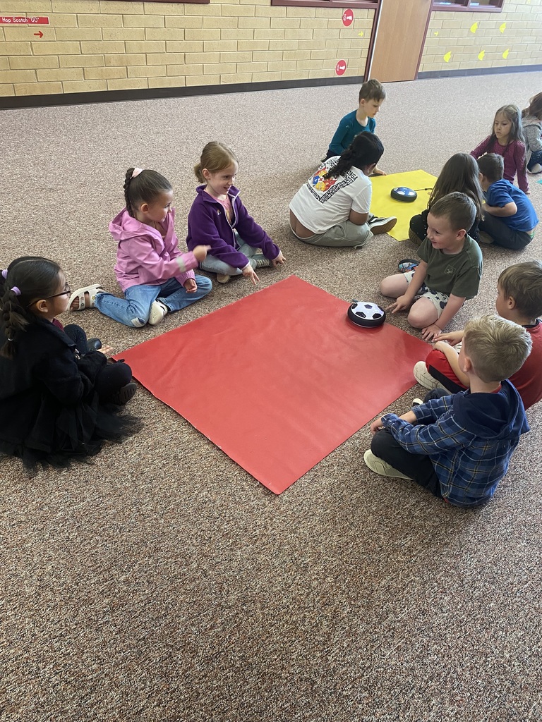 6 students sitting around a red piece of fabric with a hoverboard in the middle of them