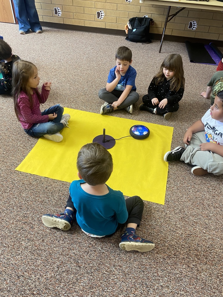 5 students sitting around a yellow piece of fabric with a hoverboard in the middle of them