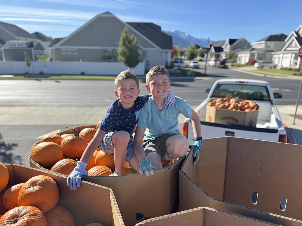 Two boys sitting on top of pumpkins in a pumpkin bin.