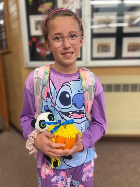 a girl holding a small pumpkin with yellow yarn attached to the top to make it look like hair as well as eyes drawn onto the pumpkin