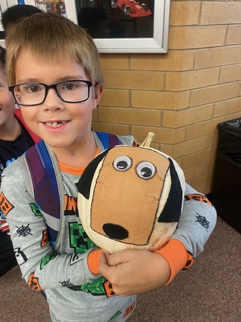 a boy wearing pajamas holding a pumpkin with a dog made out of felt attached to it