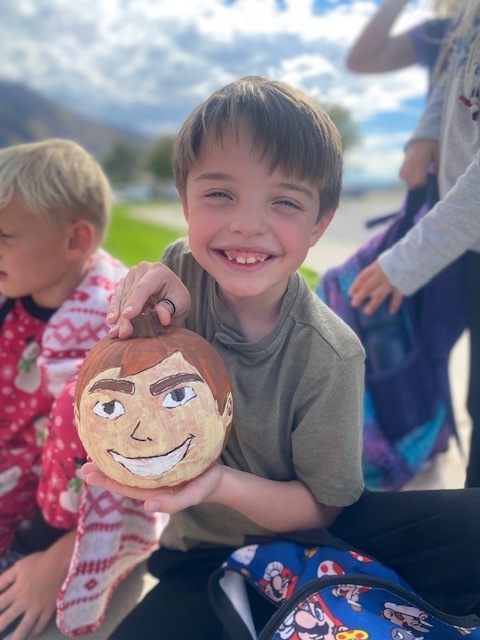 a boy holding a pumpkin that is painted to look like a head
