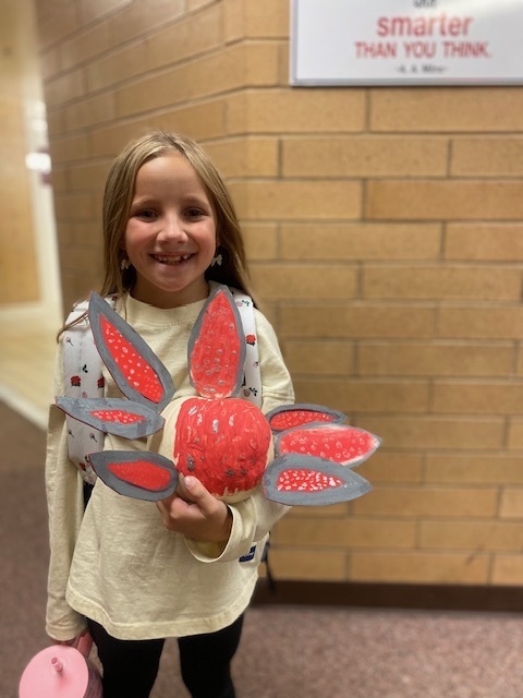 a girl holding a pumpkin with a pink cardboard feathers attached to it