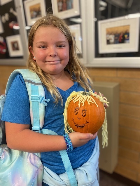 a girl holding a pumpkin with yarn attached to the top and a face drawn onto the front