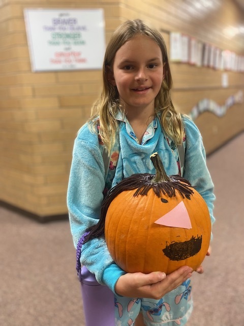 a girl holding a large pumpkin with yarn hair attached to the top and a smile drawn on with a paper nose