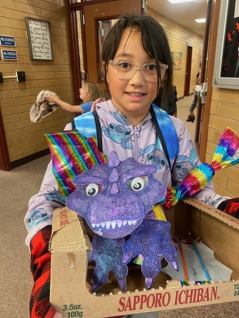 a girl holding a pumpkin that has paper attached to the front of it to look like a purple monster