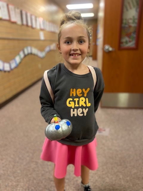 a girl holding a small pumpkin that is painted silver to look like a robot