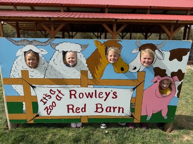 5 students with their heads through holes on a photo booth made to look like farm animals with the words "It's a zoo at Rowley's Red Barn"