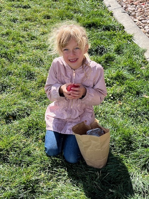 a girl kneeling down on grass and holding an apple from her lunch