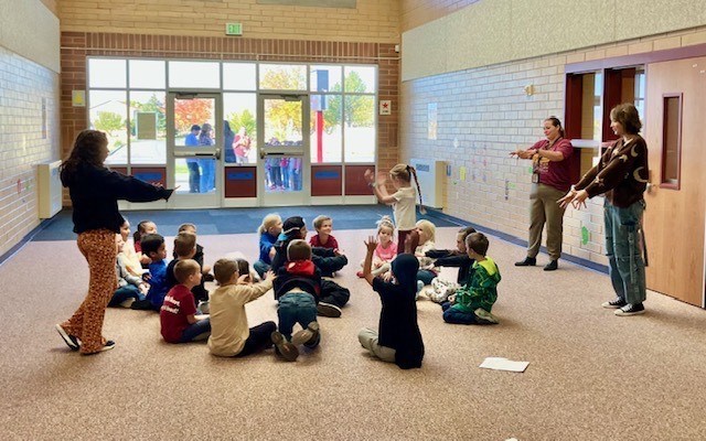 one student standing while the rest sit with their arms outstretched like a mummy 