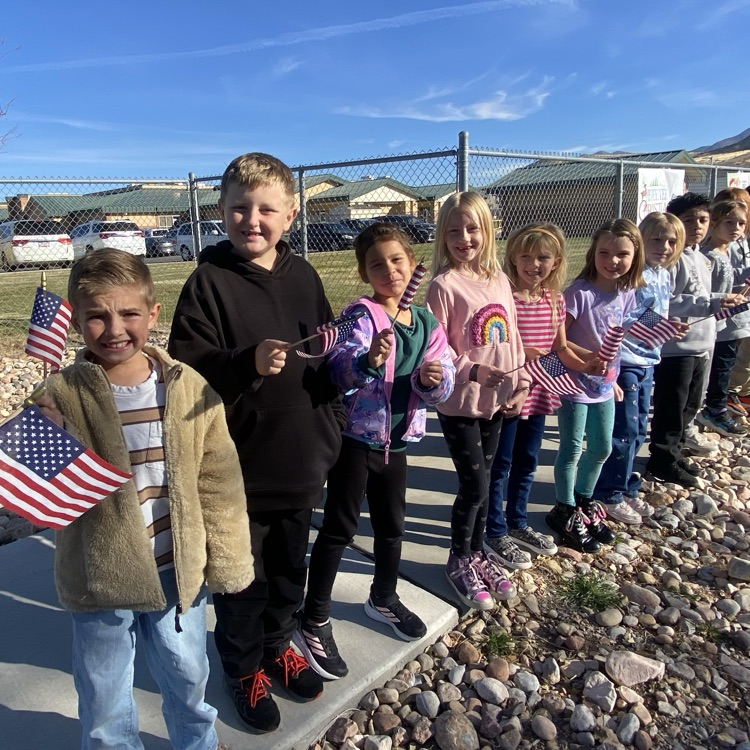 a line of second grade students standing on the sidewalk and waving flags