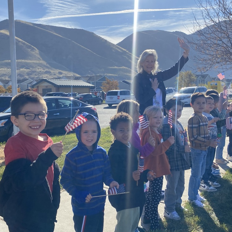 kindergarten students and an aid holding flags and waving