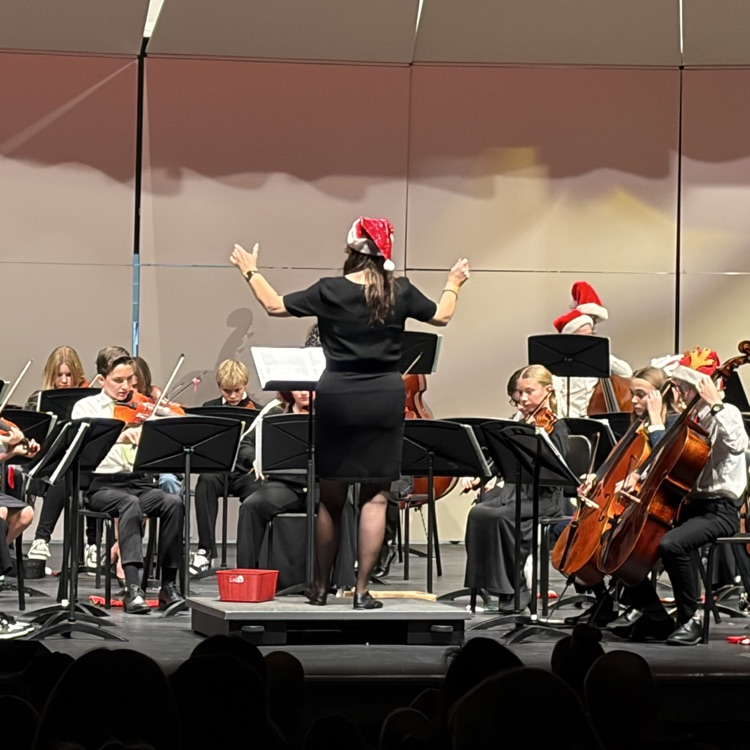teacher with arms raised directing as students play instruments