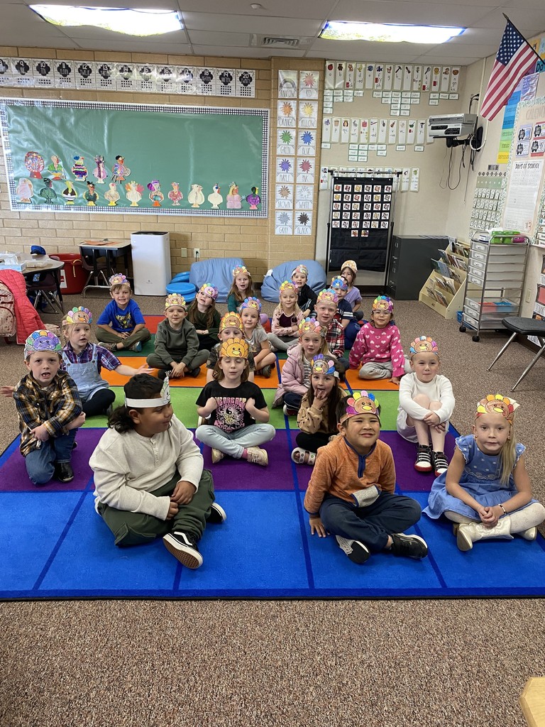 a class of kindergarten students sitting at the rug with turkey headbands on their heads
